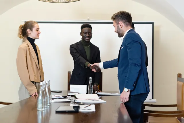 A diverse group of business professionals in a meeting room, shaking hands as a sign of agreement. Betrieb kaufen in Freiburg: Steuer- und Formfragen