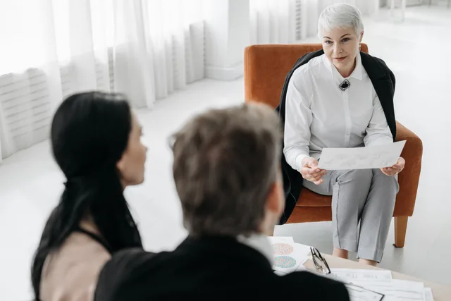 Professional advisor discussing documents with a couple in a modern office setting. Woran erkennt man eine gute Nachfolgeberatung?